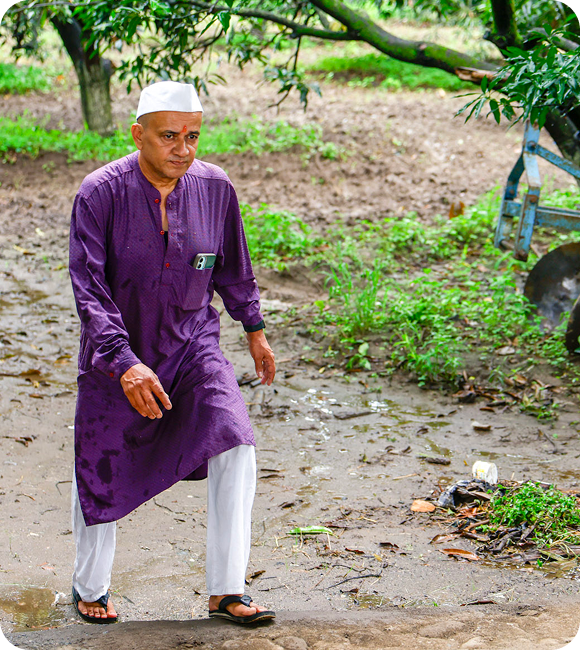 Man in a purple kurta and white cap walking along a path through Mahalaxmi Farm.