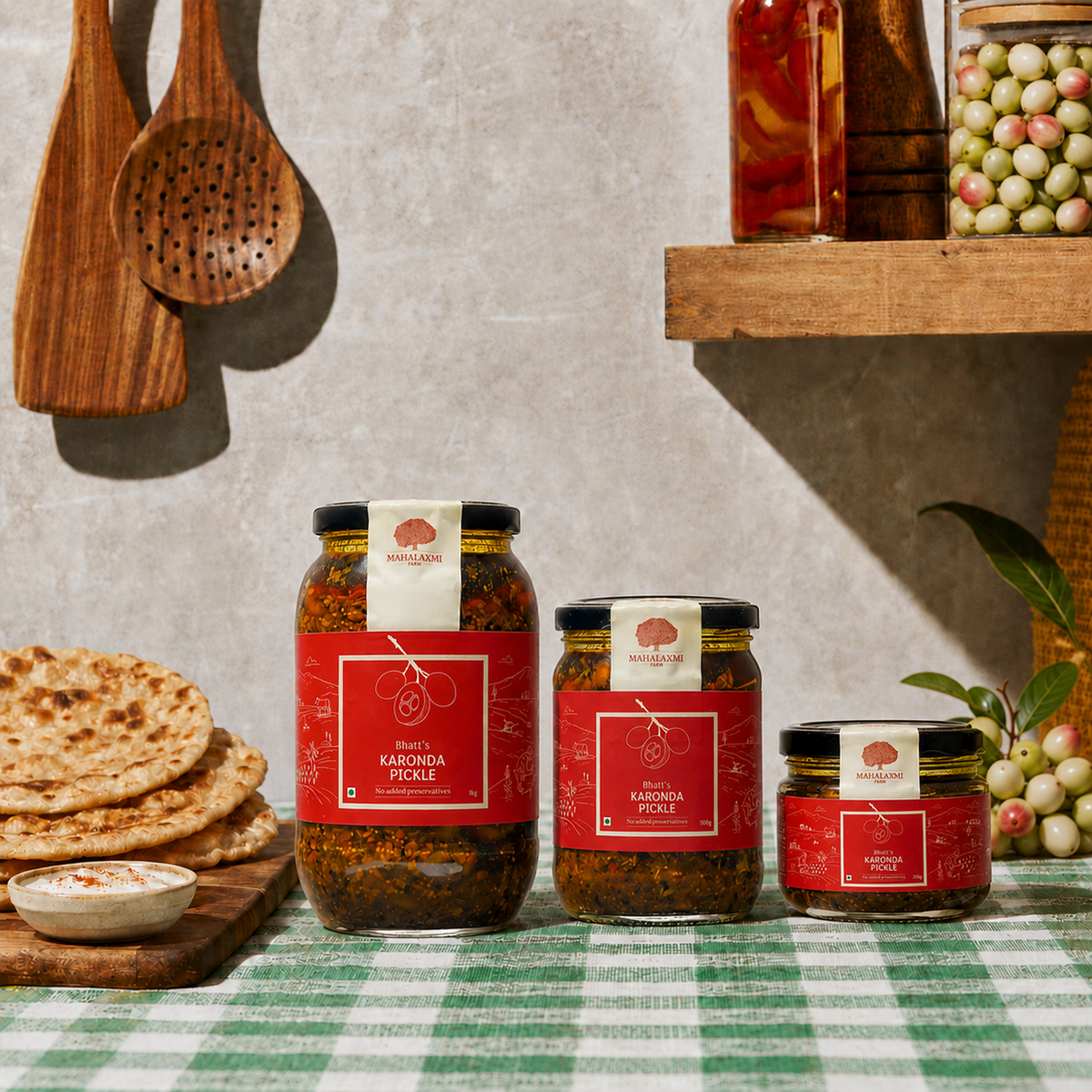 Three glass jars of Pickle in different sizes, arranged on a green and white checkered tablecloth with flatbread and kitchen utensils in the background.