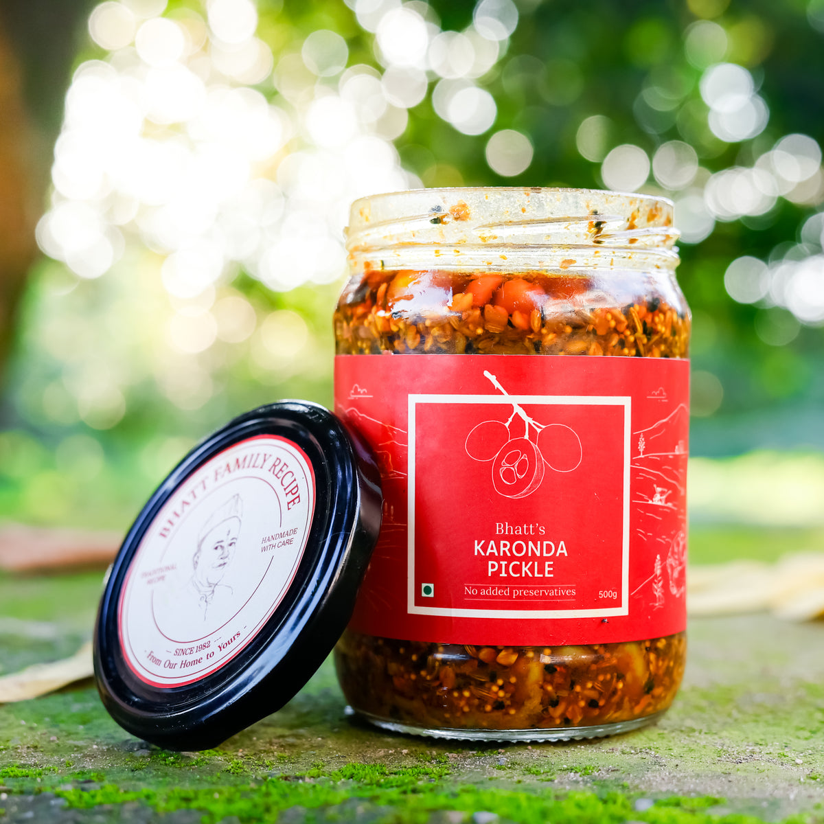 Open jar of Bhatt’s Karonda Pickle with a red label and its lid resting beside it outdoors.