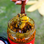 Spoon lifting karonda berries and spices from an open jar of Karonda Pickle.