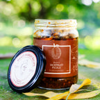 Open jar of Bhatt’s Jackfruit Pickle with its brown label and lid resting beside it outdoors.