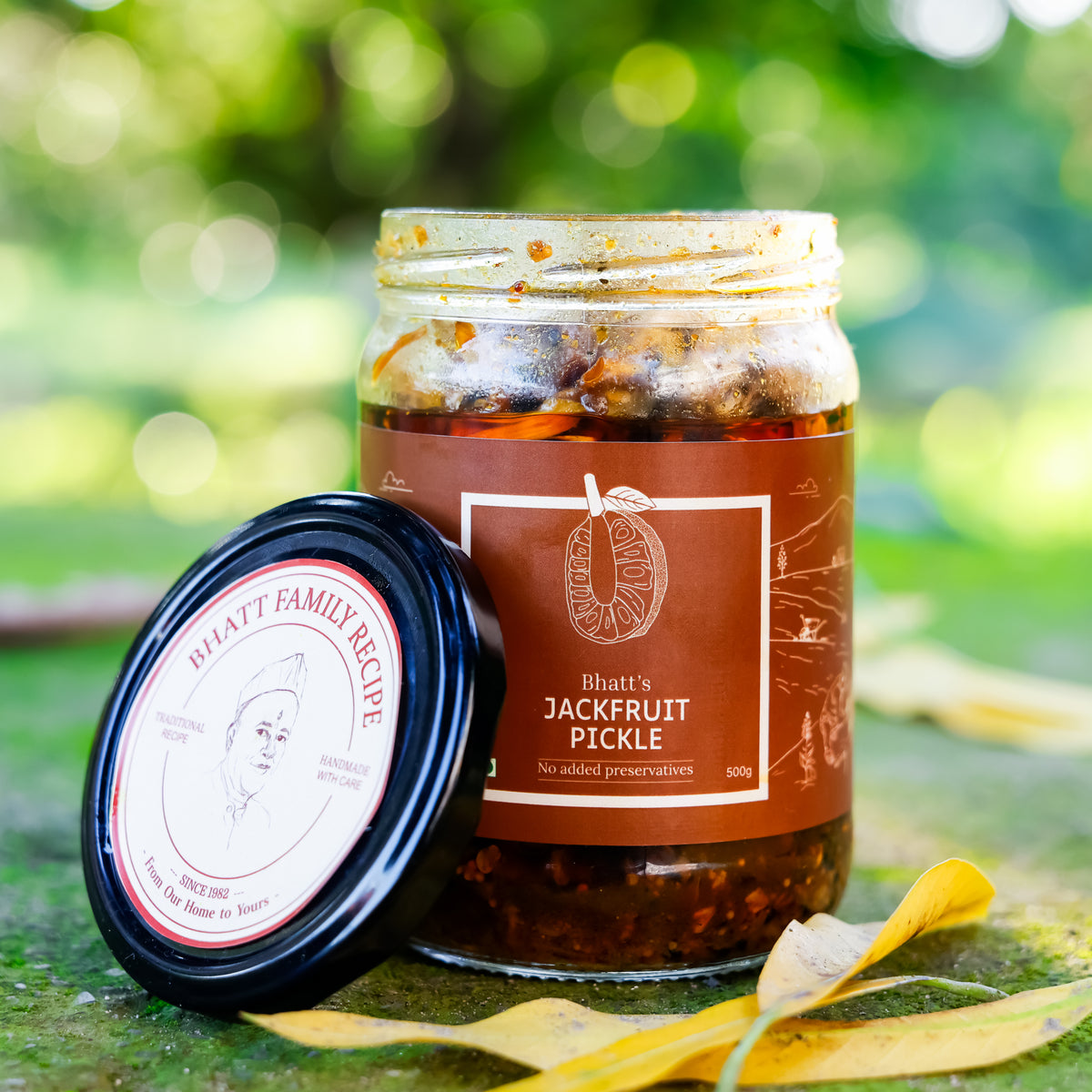 Open jar of Bhatt’s Jackfruit Pickle with its brown label and lid resting beside it outdoors.
