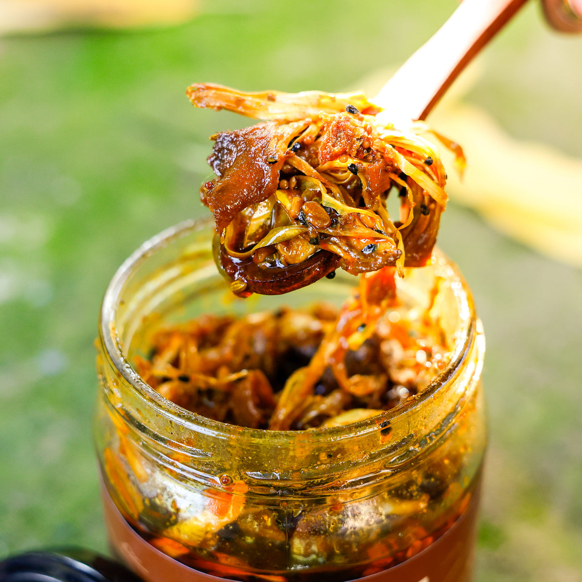 Spoon lifting jackfruit pieces and spices from an open jar of Jackfruit Pickle.