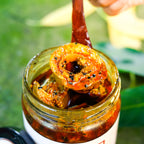 Spoon lifting a ring of mango coated in spices from an open jar of Ring Shaped Mango Pickle.