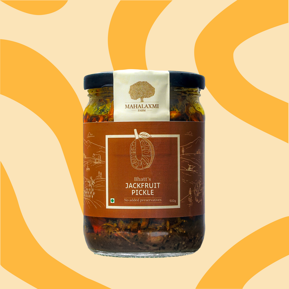A glass jar of Mahalaxmi Farms Jackfruit Pickle' with a brown label and black lid, set against a warm beige background with yellow wavy patterns.