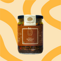 A glass jar of Mahalaxmi Farms Jackfruit Pickle' with a brown label and black lid, set against a warm beige background with yellow wavy patterns.