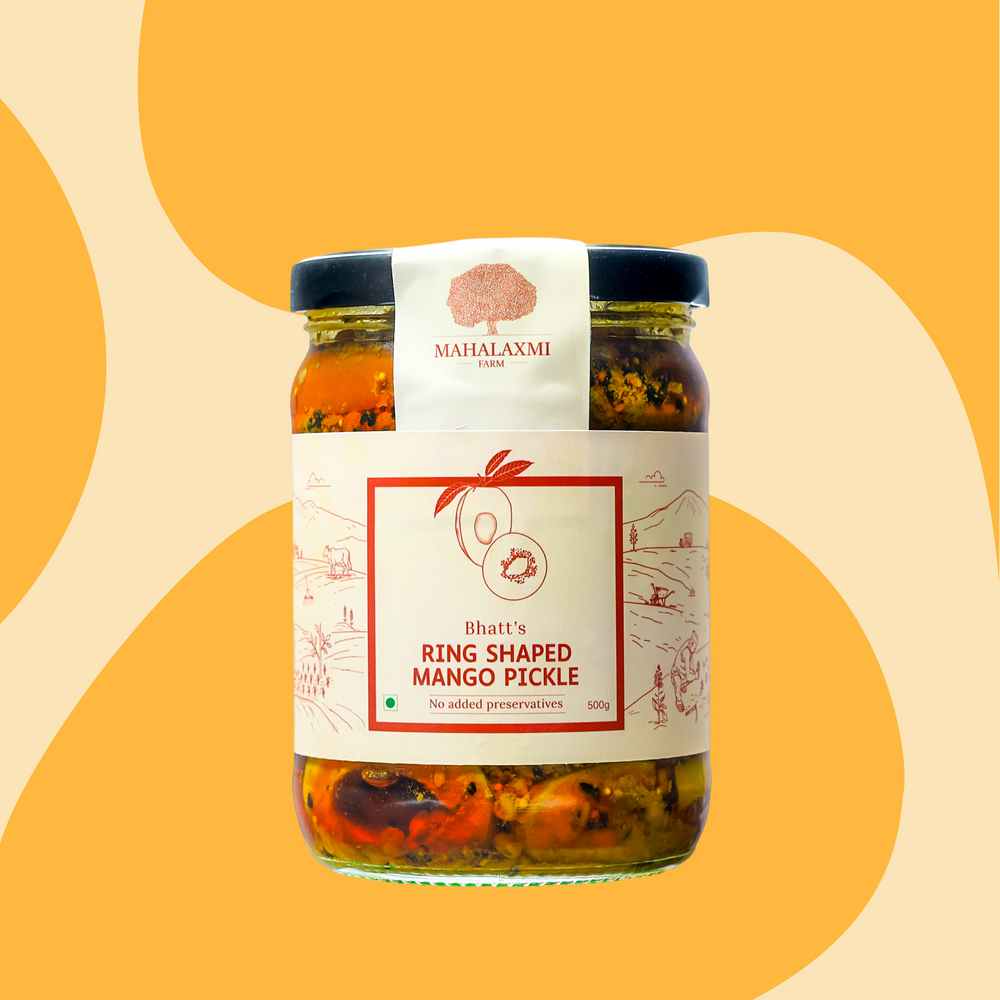A glass jar of Bhatt's Ring Shaped Mango Pickle by Mahalaxmi, featuring a white label with red text and illustrations, set against a warm yellow and beige abstract background.