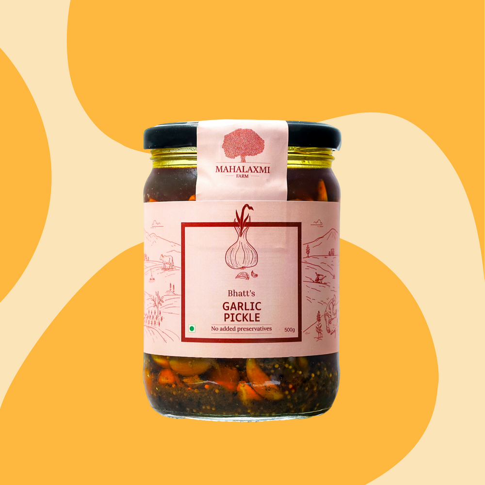 A glass jar of Bhatt's Garlic Pickle by Mahalaxmi Farm, featuring a pink label and a black lid, set against a warm yellow and beige abstract background.