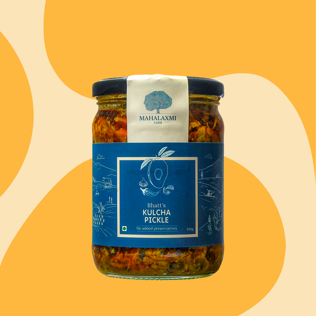 A glass jar of Bhatt's Kulcha Pickle by Mahalaxmi Farm, featuring a dark blue label and a white top seal, set against a warm yellow and beige abstract background.