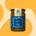 A glass jar of Bhatt's Kulcha Pickle by Mahalaxmi Farm, featuring a dark blue label and a white top seal, set against a warm yellow and beige abstract background.