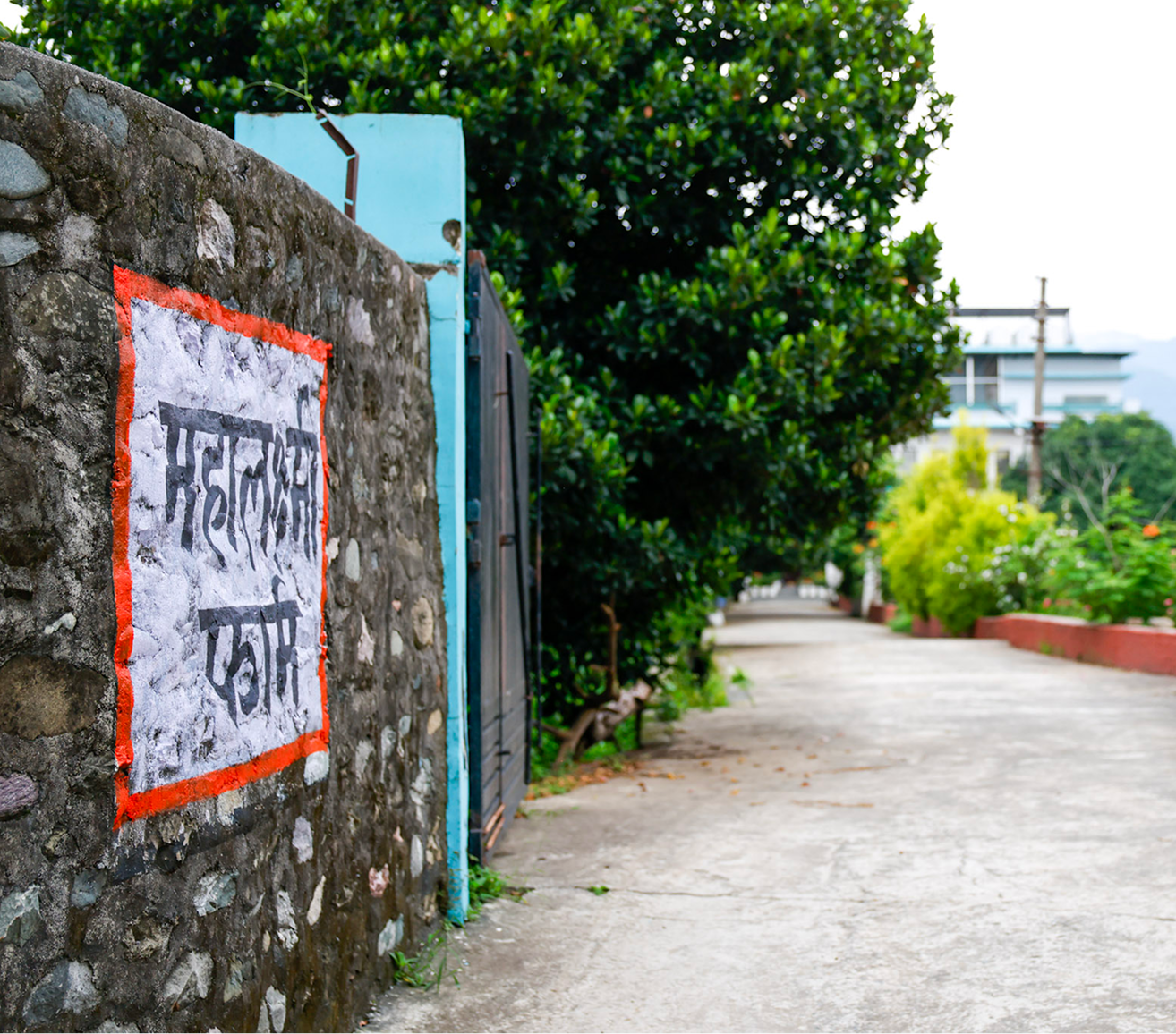 Entrance to Mahalaxmi Farm with a Hindi sign on a stone wall beside a tree-lined path.